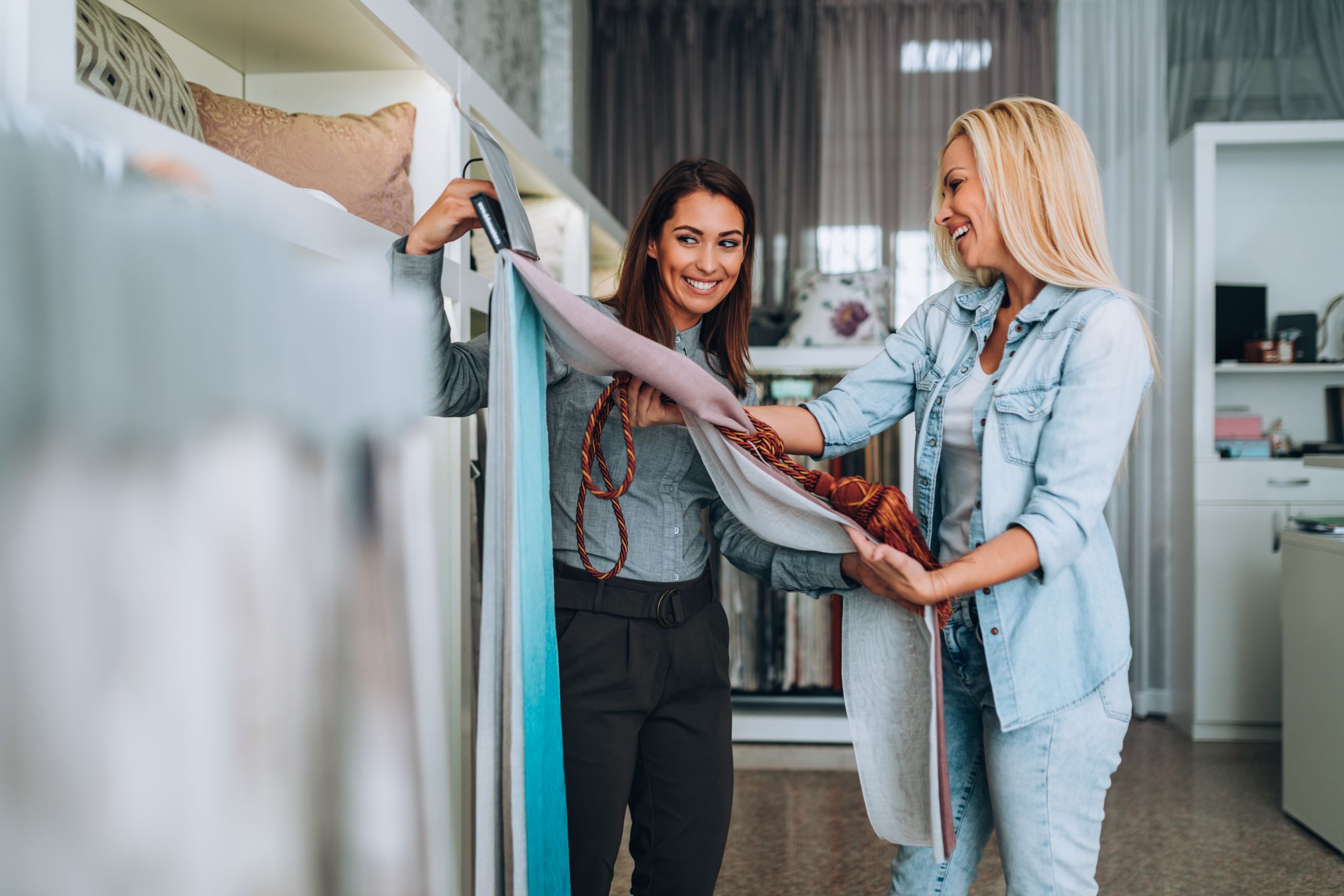 Young woman designer talking with a saleswoman and chooses fabrics for curtains in textile show room.